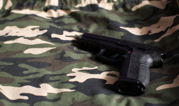 istock Black handgun, firearm on camouflage army green fabric 1350585940