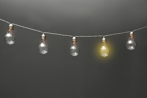 Idea concept. Garland of light bulbs with one glowing on grey background