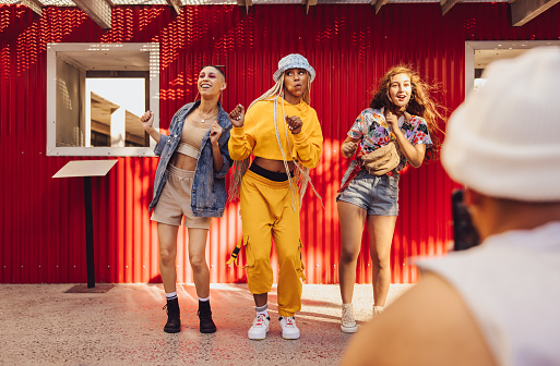 Following fun social media trends. Group of generation z friends doing trendy dance moves in front of a camera phone. Vibrant young people creating content for their social media vlog.