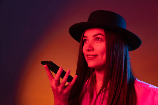 istock One young beautiful girl wearing black hat using phone isolated on dark studio background in neon light. Concept of emotions, fashion 1350588917