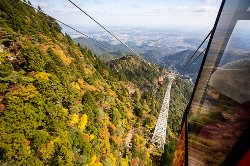 A woman looking out of the window of a cable car ropeway to the mountain tree autumn colors.