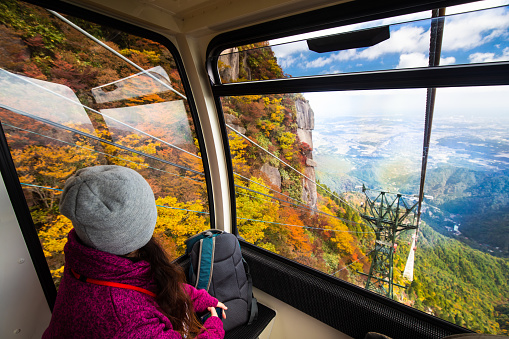 A woman looking out of the window of a cable car ropeway to the mountain tree autumn colors.