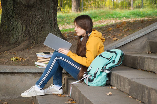 dziewczyna w wieku 13 lat siedzi na schodach i czyta książkę w parku, idzie na egzaminy szkolne. - book child staircase steps zdjęcia i obrazy z banku zdjęć