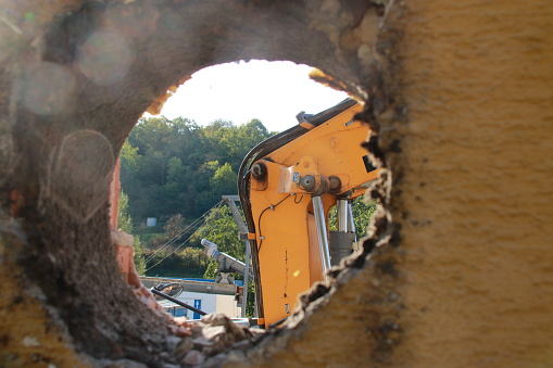 Arm of an excavator photographed through an opening in the wall