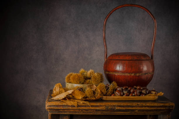 bodegón de castañas y frutos de castaña sobre mesa de madera sobre fondo negro - vanitas fotografías e imágenes de stock