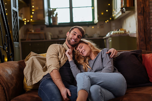 Beautiful young couple hugging while sitting on their living room sofa