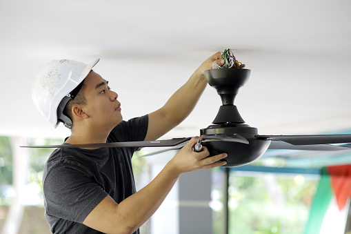 An Asian man is changing ceiling fan at residence.
