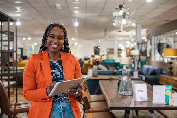 Confidence In The Workplace A medium close-up portrait of a confident retail worker in her place of work in Newcastle upon Tyne in the North East of England. She is standing holding a digital tablet. assistant stock pictures, royalty-free photos & images