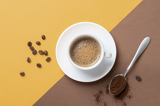 Flat lay composition of cup of coffee on brown and yellow background.