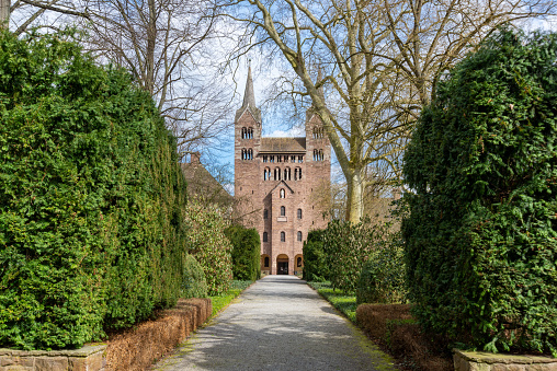 Höxter, Nordrhein-Westfalen-Germany - 04-04-2021: The hedge-lined entrance to the Westwerk of Corvey Castle in Höxter with sun and not yet leafy trees and blue sky.