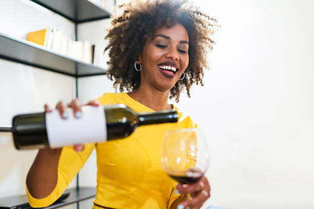 a smiling african woman pours wine into her goblet - wine bottle wine residential structure alcohol imagens e fotografias de stock