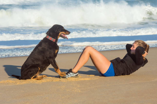 beautiful young woman doing sit-ups on the sand with the help of her dog