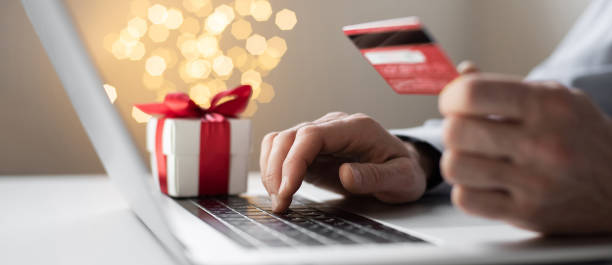 hombre ordenando regalos de navidad usando computadora portátil y tarjeta de crédito. compras en línea durante las vacaciones - holiday shopping fotografías e imágenes de stock