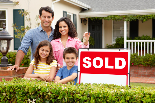 Hispanic family standing outside home smiling with sold sign