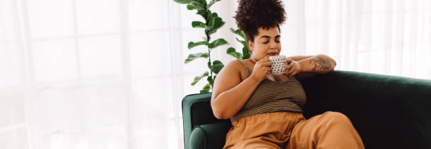 istock Woman sitting on sofa and drinking coffee 1350610765