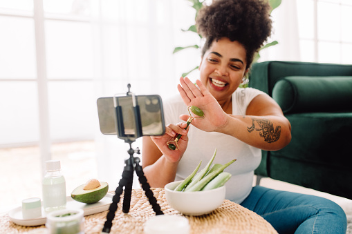 Woman showing how to use jade roller tool while recording a vlog. Female holding beauty tool on her palm while recording video for her channel.