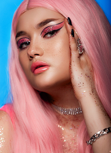Plus size fashion model, beauty woman with professional makeup glitter on the body and pink hairstyle on blue background, closeup studio shot