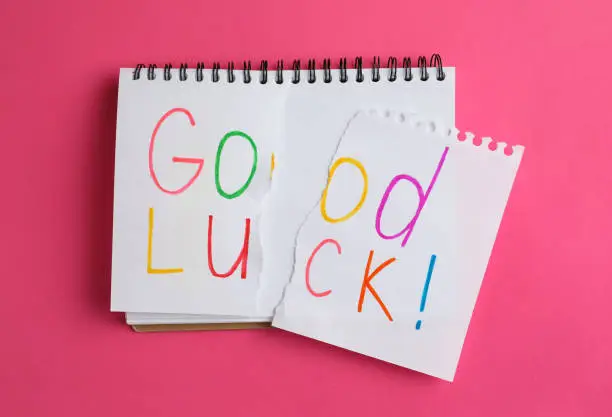 Photo of Torn phrase GOOD LUCK written in notebook on pink background, top view