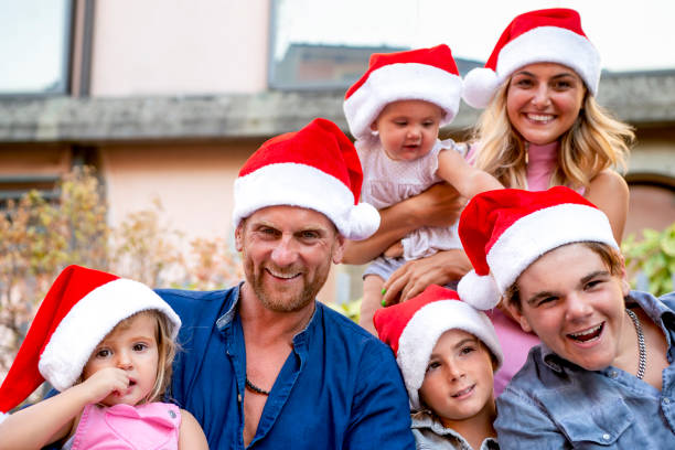 merry christmas! young large family portrait celebrating xmas wearing a santa hat outdoors. parents and children close up during winter warm festivities. family time on summer vacation holiday concept - babies and children close up horizontal looking at camera imagens e fotografias de stock
