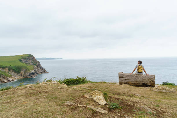 istock Adventurous caucasian man isolated sit on a cliff bench. 1350624463
