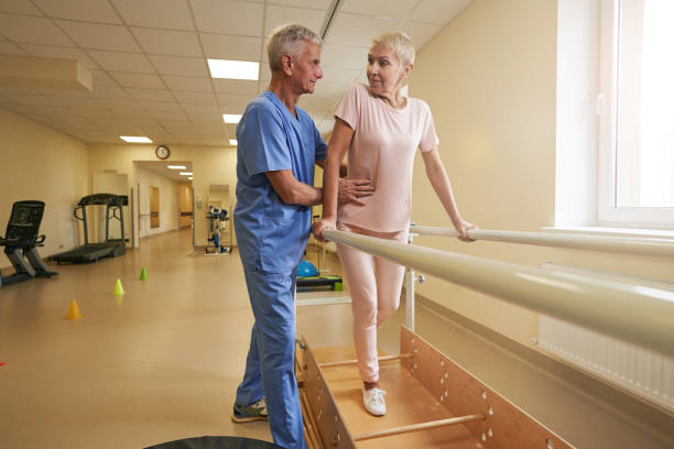 istock Mature female walking between parallel bars in rehabilitation room 1350626478