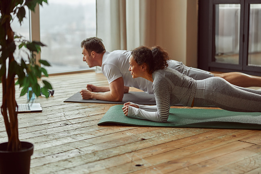 Athletic man and woman are doing core workout at home while watching online video on notebook