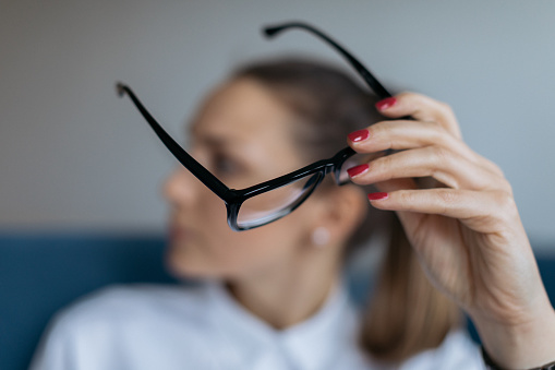 An out of focus young Caucasian businesswoman working remotely from home, holding her reading glasses