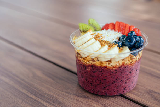 Close-Up Shot of a Healthy Acai Food Bowl on a Wooden Table Outdoors in the Summer Close-Up Shot of a Healthy Acai Food Bowl with Bananas, Blueberries, Kiwi, Strawberries, Granola, and Bee Pollen on a Wooden Table Outdoors in the Summer with Copy Space and Artistic Bokeh. Acai Bowl stock pictures, royalty-free photos & images