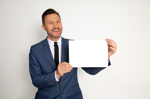 Young handsome brunet laughing man holding white empty board. Ceo, manager, Businessman showing poster for advertising. Studio shot on white background