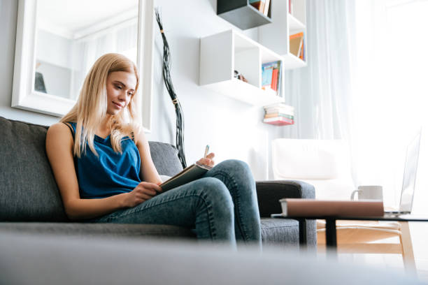 istock Woman sitting on sofa and writing in notepad at home 1350632239