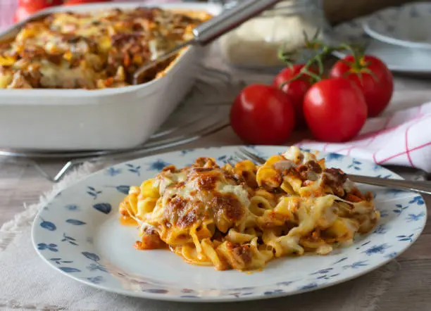 Homemade fresh cooked traditional italian pasta casserole with bolognese and bechamel sauce, topped with mozzarella and parmesan cheese and served on a plate with table background.