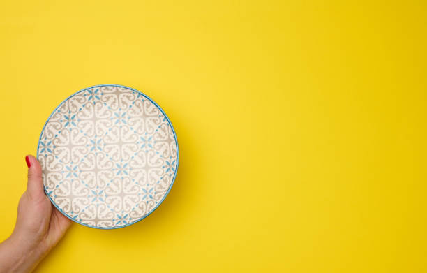 istock female hand holding an empty round plate on a yellow background, top view 1350633815