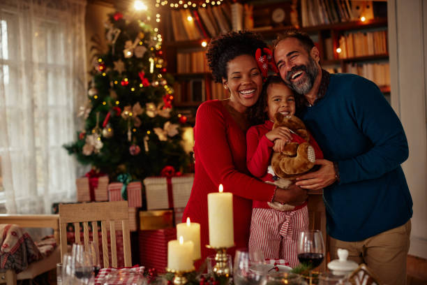 Diverse family have a dinner christmas party at home. Mixed race parents and daughter standing around dining table, hugging, smiling and enjoying holiday together family christmas stock pictures, royalty-free photos & images
