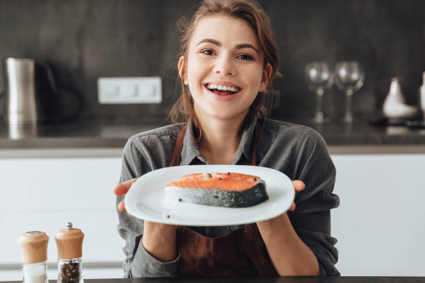 istock Happy woman standing in kitchen while cooking fish. 1350637329