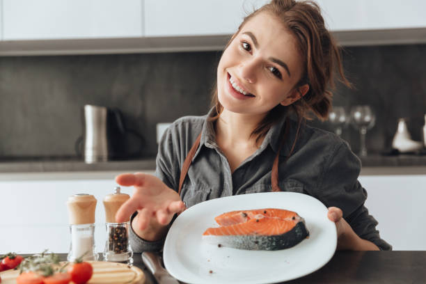 istock Pretty woman standing in kitchen while cooking fish. 1350637547