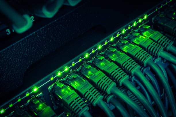 パッチコードで接続されたデータセンターから暗闇の中で輝く黒いスイッチまで、緑のネットワークケーブルをクローズアップ - cable network server network connection plug green ストックフォトと画像