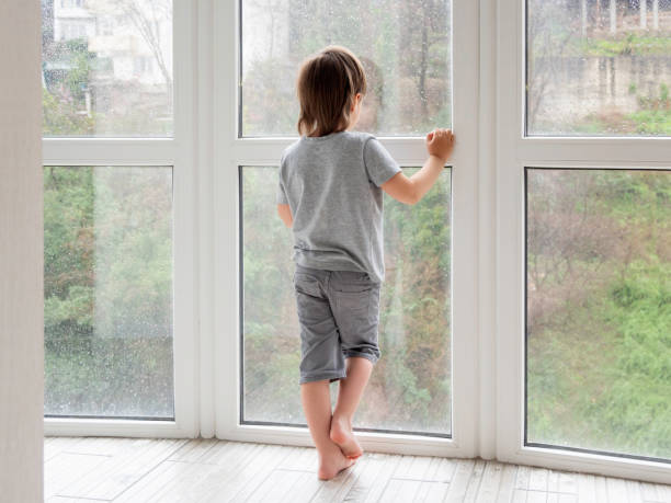 istock Little boy looks outdoors through wet panoramic window with raindrops. Coronavirus COVID19 quarantine. Rainy summer weather. Kid stays alone at home. Loneliness and sad mood without children's company. 1350646986