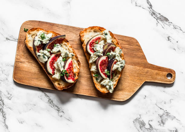 Gorgonzola cheese, figs, thyme, honey bruschetta on a cutting board on a light background, top view Gorgonzola cheese, figs, thyme, honey bruschetta on a cutting board on a light background, top view plate fig blue cheese cheese stock pictures, royalty-free photos & images