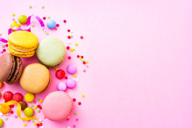 Top view of multi colored macaroons and candies shot on pink background. The composition is at the left of an horizontal frame leaving useful copy space for text and/or logo at the right. High resolution 42Mp studio digital capture taken with SONY A7rII and Zeiss Batis 40mm F2.0 CF lens