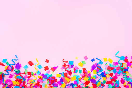 Celebration, party or birthday backgrounds: multi colored confetti arranged at the bottom border of a pink background making a frame and leaving useful copy space for text and/or logo. High resolution 42Mp studio digital capture taken with SONY A7rII and Zeiss Batis 40mm F2.0 CF lens