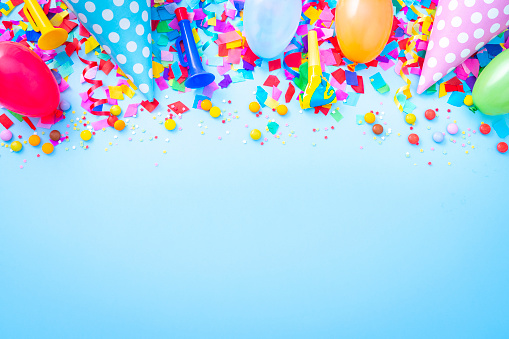 Celebration, party or birthday backgrounds: multi colored party accessories like balloons, steamers, confetti and candies arranged at the top border of a blue background making a frame and leaving useful copy space for text and/or logo. High resolution 42Mp studio digital capture taken with SONY A7rII and Zeiss Batis 40mm F2.0 CF lens