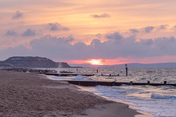 A scenic view of a beautiful sunrise at the beach with some hill in the background A scenic view of a beautiful sunrise at the beach with some hill in the background hengistbury head photos stock pictures, royalty-free photos & images