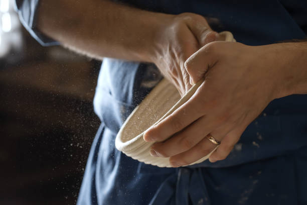 istock Male baker lightly flouring proofing basket for home made sourdough bread. 1350649190