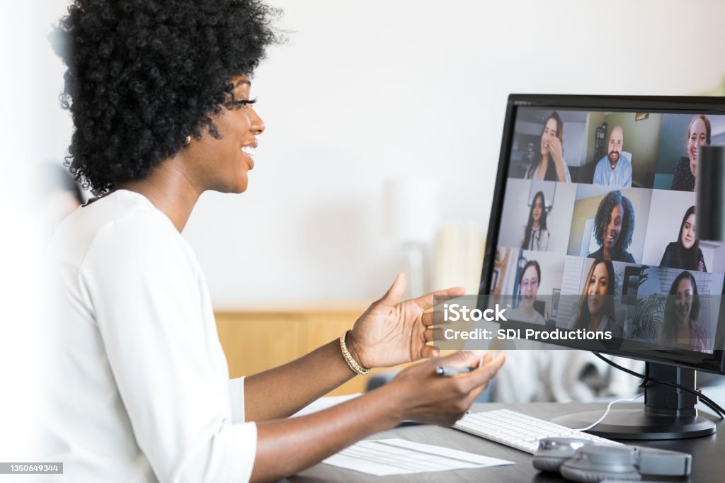 Female financial advisor gestures during meeting with company employees Smiling and gesturing during a meeting with the company's employees, the mid adult female financial advisor reviews the numbers on the spreadsheet in front of her. Video Call Stock Photo