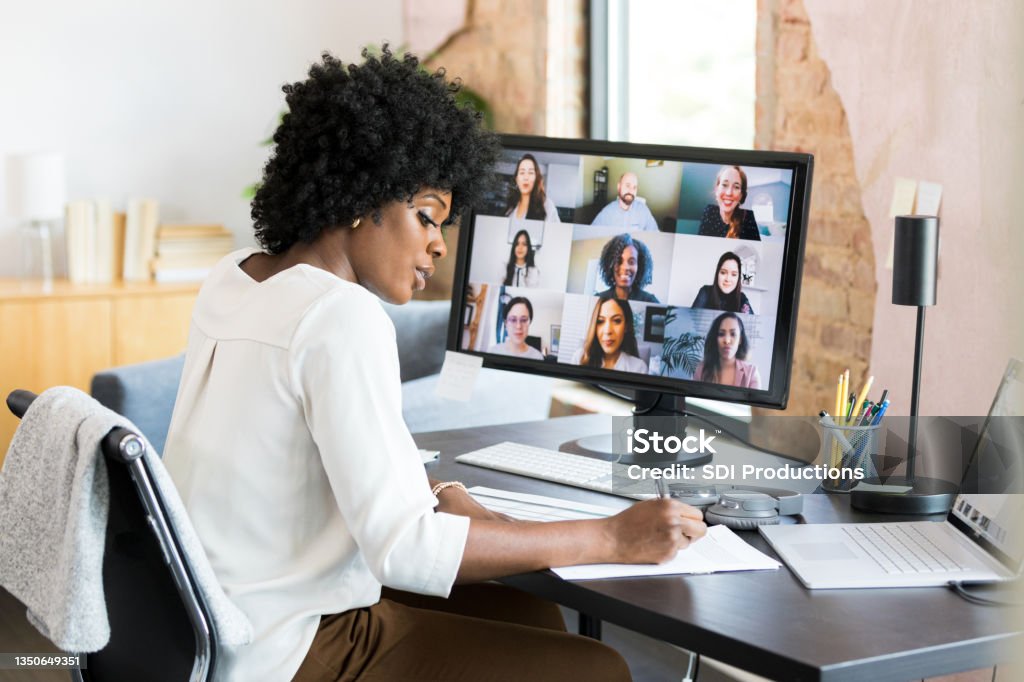 Mid adult female CEO takes notes during employee engagement meeting The mid adult female CEO takes notes during the meeting with the diverse employees in her company.  She is sitting at her desk and using her laptop and desktop PC. Desktop PC Stock Photo