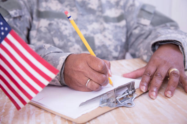 Female recruiter reviews applications.   Senior soldier reviews paperwork  sits at desk.  Cup of American Flags on her desk.