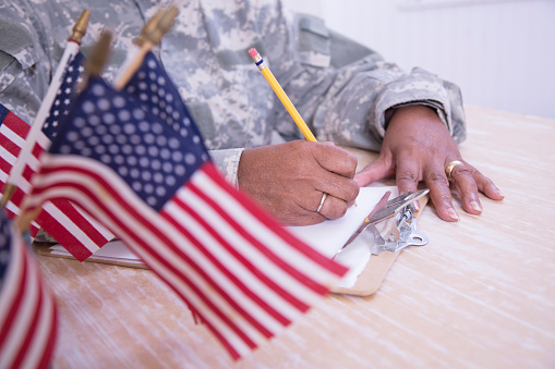 Female recruiter reviews applications.   Senior soldier reviews paperwork  sits at desk.  Cup of American Flags on her desk.
