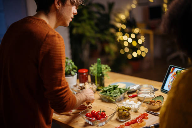 joven mirando la tableta digital y hablando con su novia mientras prepara pizza para la cena - vegetarian pizza fotografías e imágenes de stock