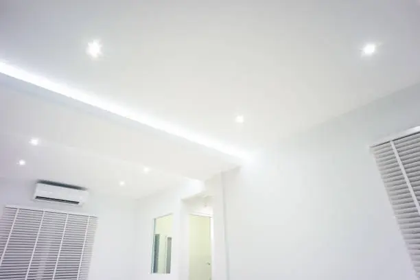 LED strip light and illumination. Also called ribbon light or LED tape. That suspended on ceiling and hide in plasterboard in empty living room include down light, white wall, window, air conditioner, adjusting vertical or venetian blinds. That is modern luxury interior home building design and technology.