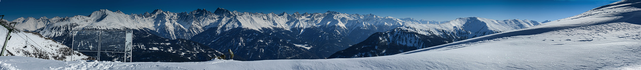 Panorama with snowy mountains in Austrian Alps with snow in foreground with a viewpoint next to a chairlift